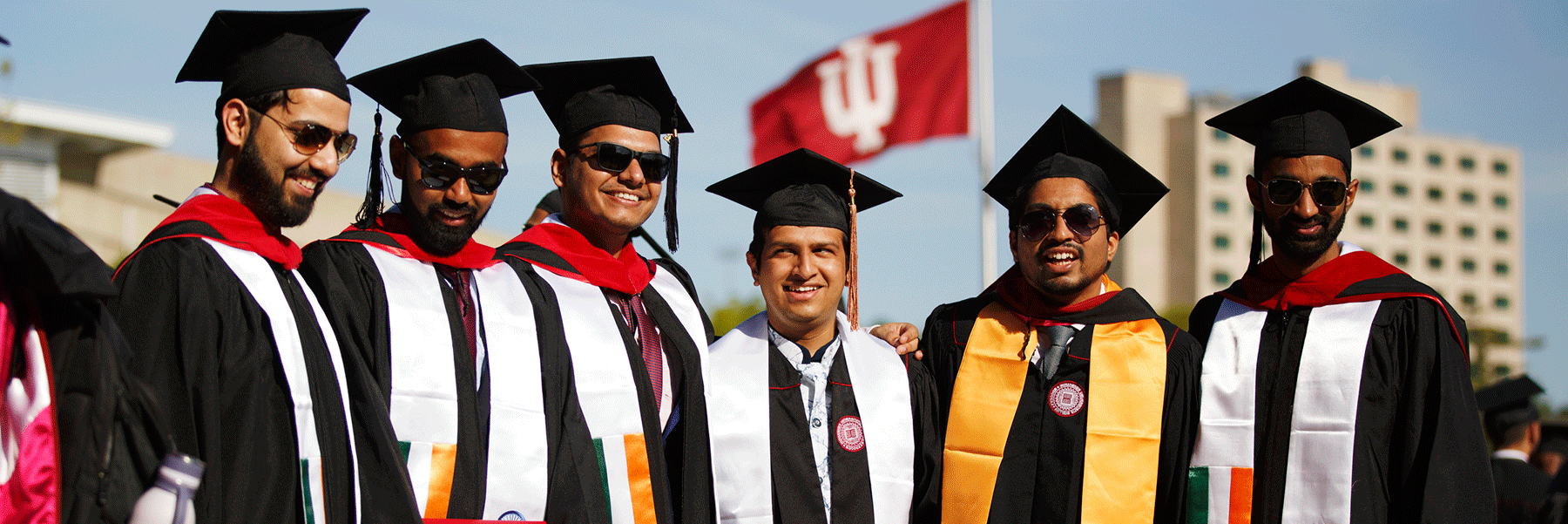 A group of male graduates standing in a line and smiling.