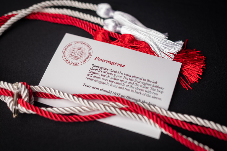 A highly attractive photo of silky white and crimson honor cords arranged around a card with the university seal, describing their use. 